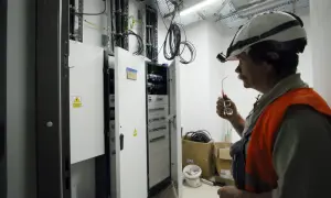 Elektryk w kasku i kamizelce odblaskowej przy skrzynce elektrycznej.